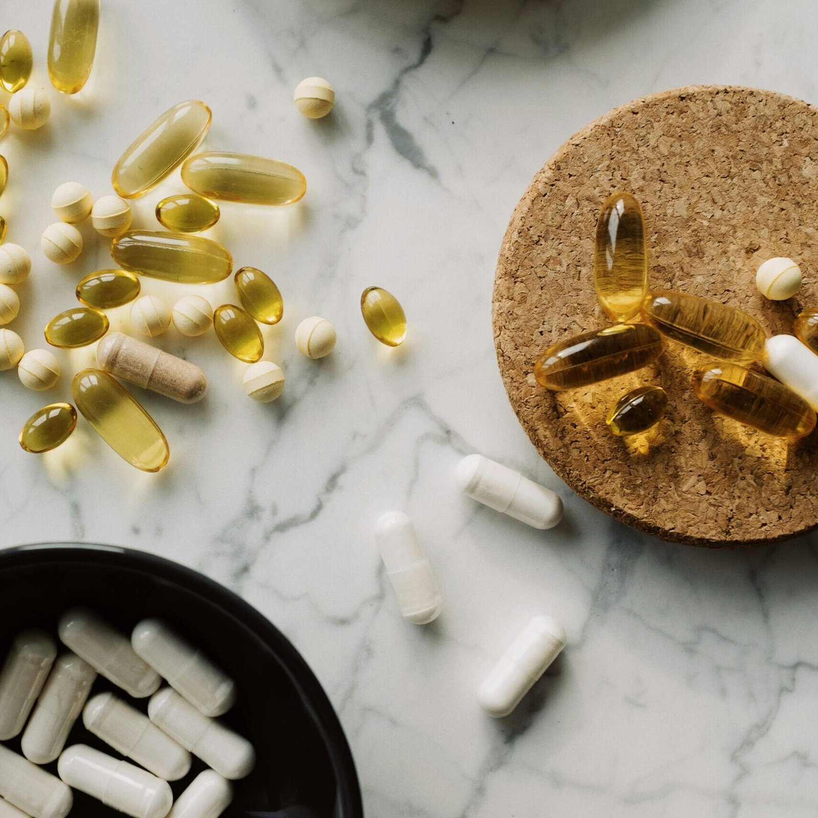 From above of mixed white vitamins and omega placed in black bowl on cellulose stand and scattered around the table